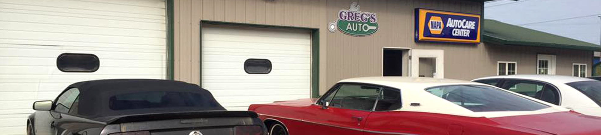 Exterior of Greg's Auto shop in Le Center with a mix of new, old, and classic cars parked in front of the auto bay doors